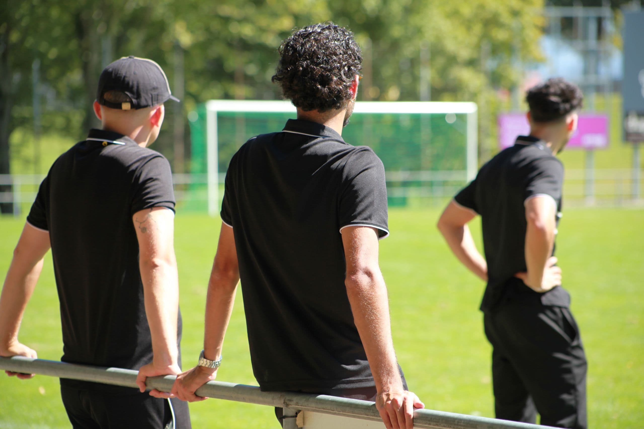 Trois entraîneurs accoudés à la barrière, face au terrain