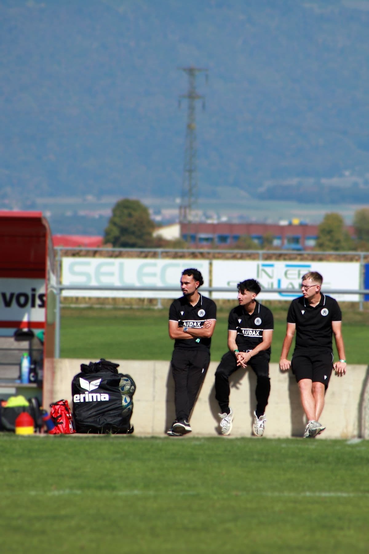 Trois membres du staff assis sur le muret au bord du terrain
